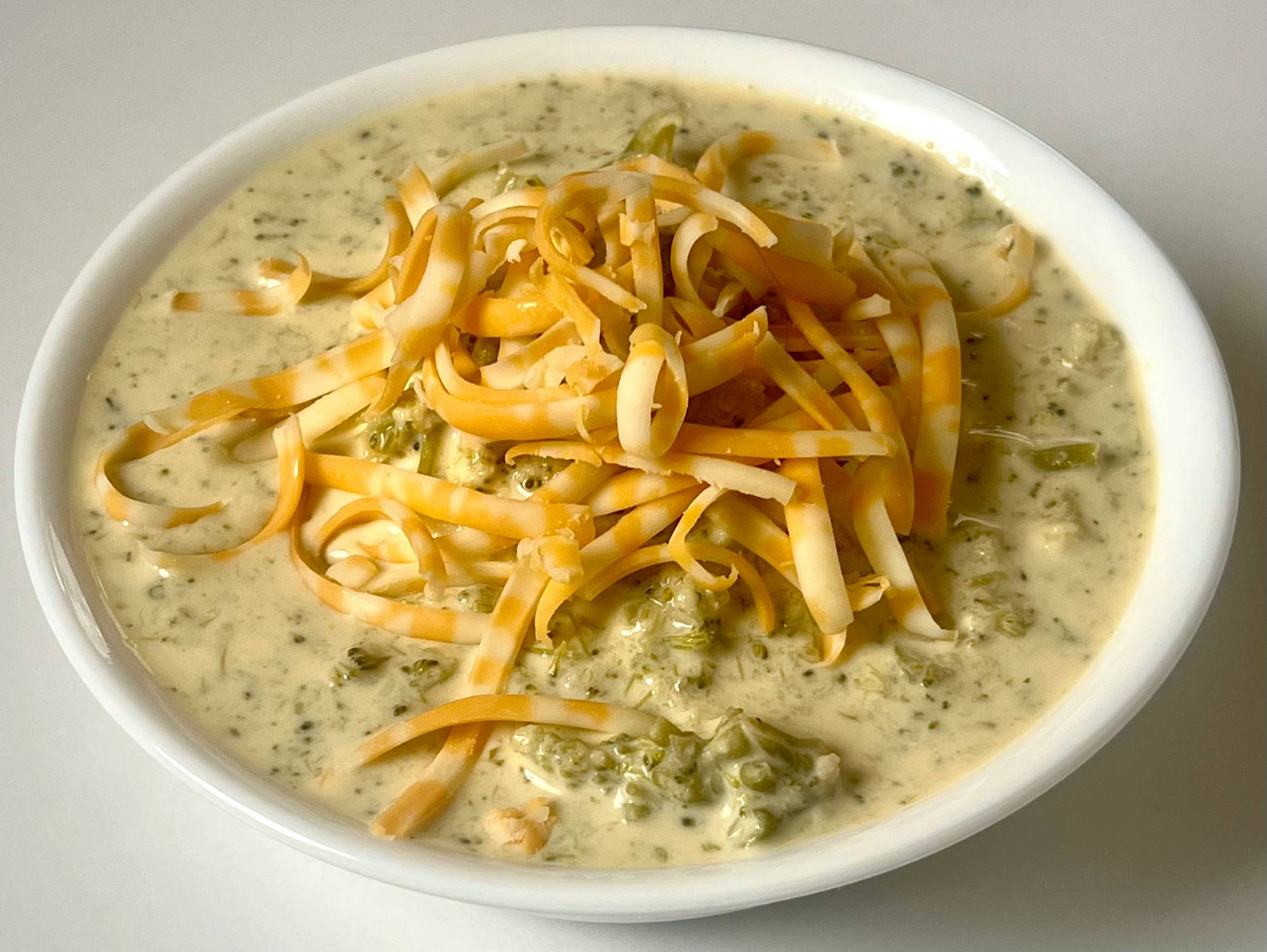 Creamy keto broccoli cheddar soup topped with shredded cheese in a white bowl