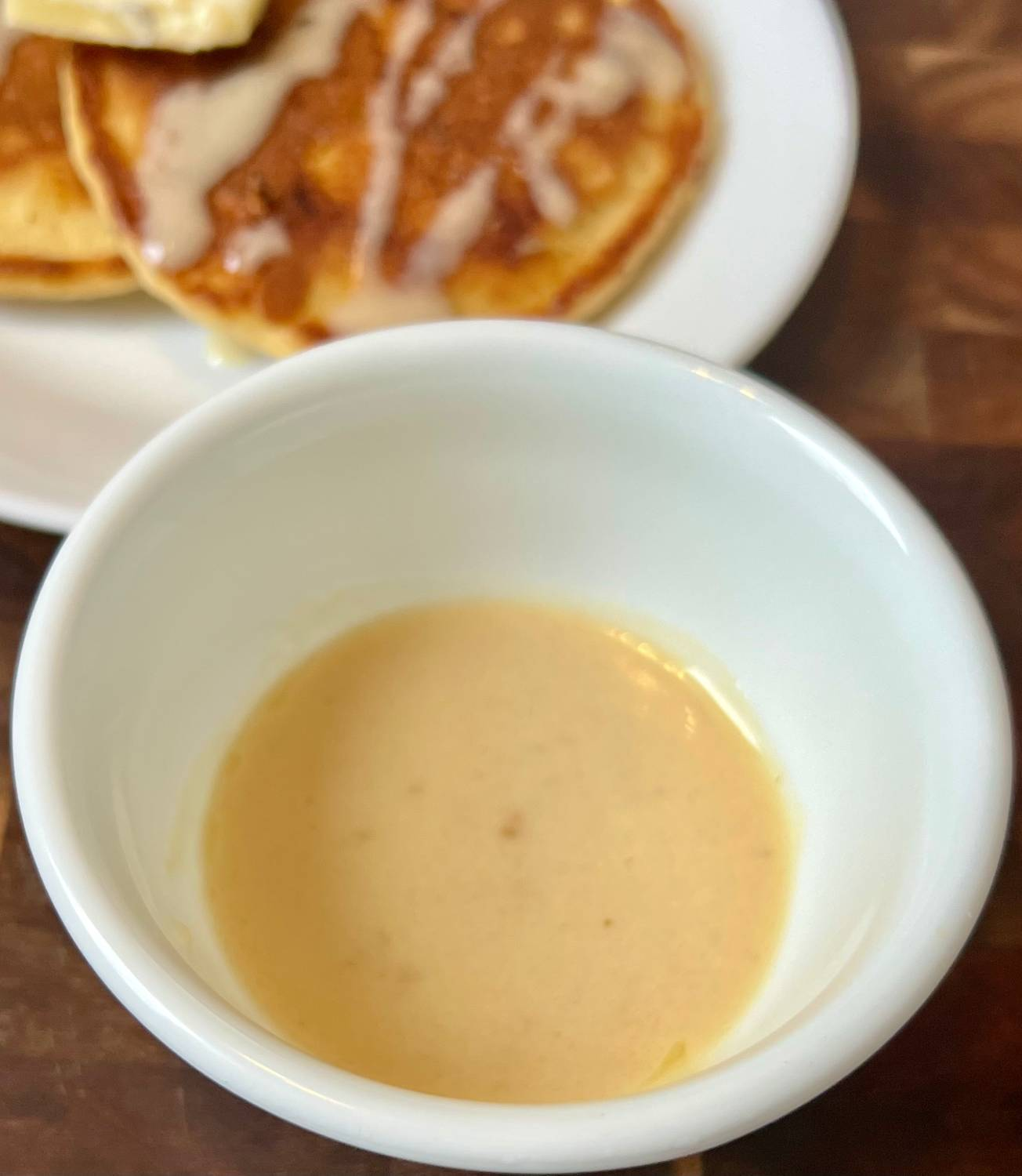 Homemade keto syrup in a white bowl with almond flour pancakes in the background