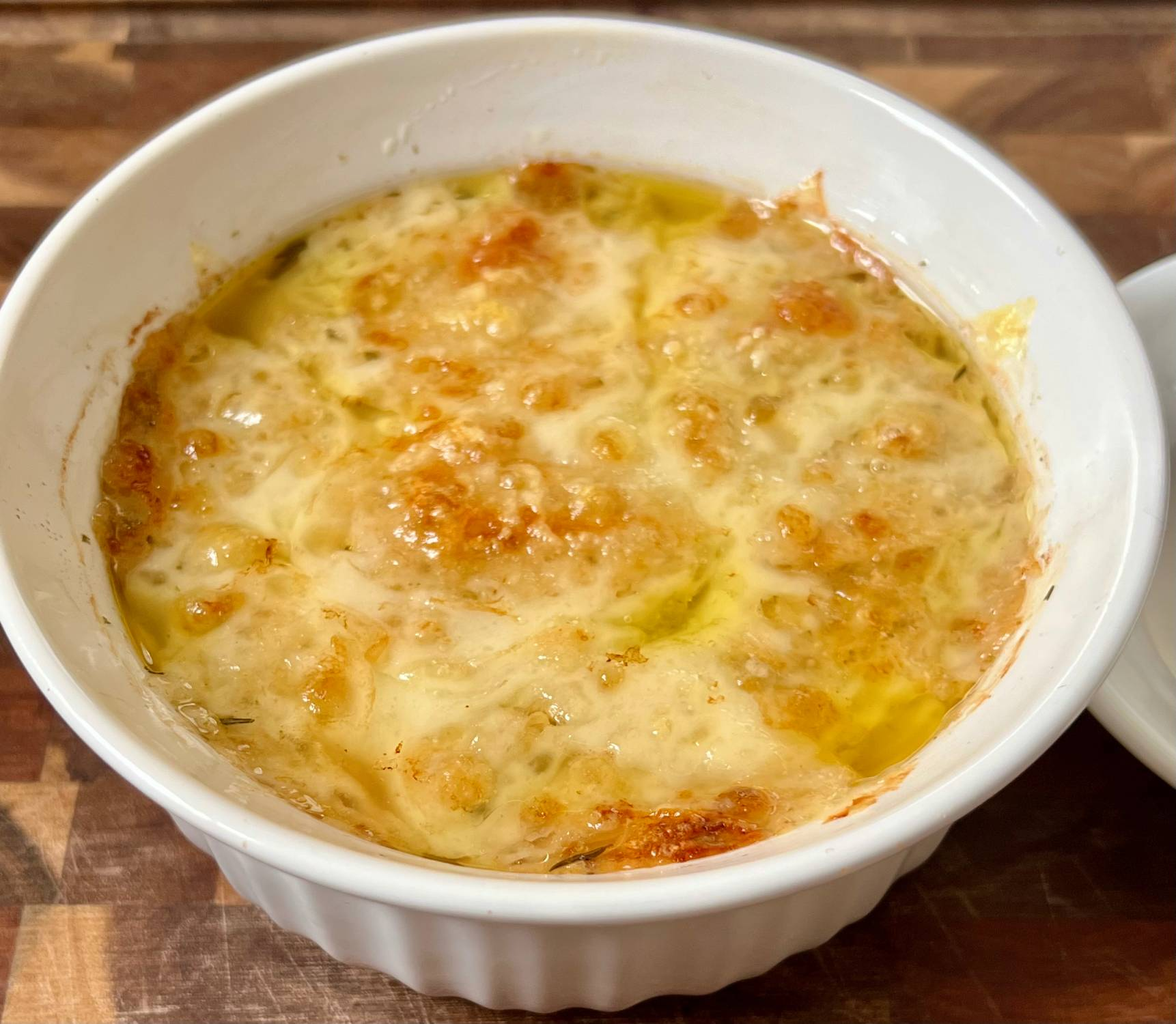 Broiled keto French onion soup with melted cheese in a white oven-safe bowl