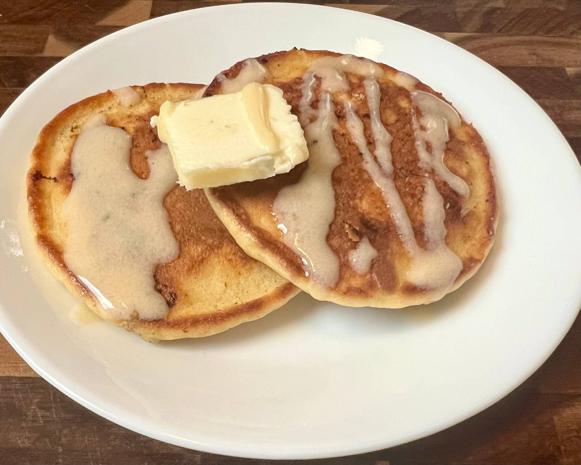 Keto almond flour pancakes topped with butter and homemade sugar-free syrup on a white plate
