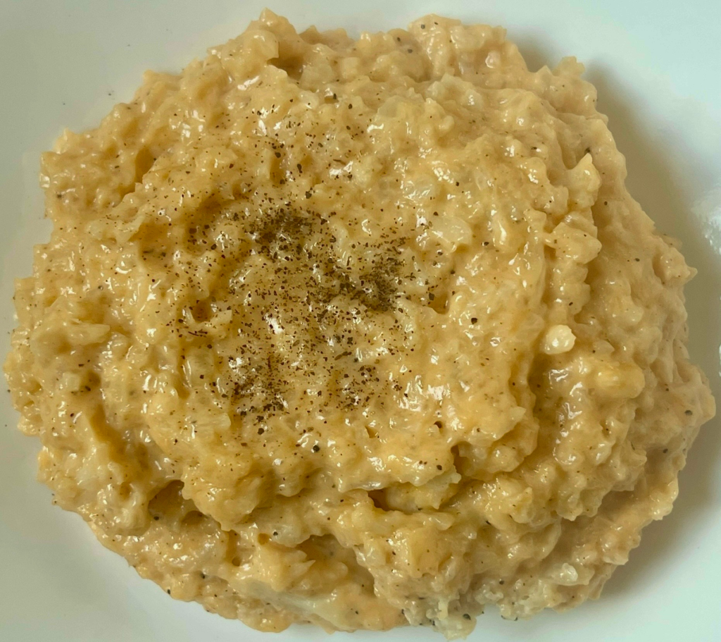 Close up of creamy keto cheesy cauliflower rice with melted cheddar and black pepper