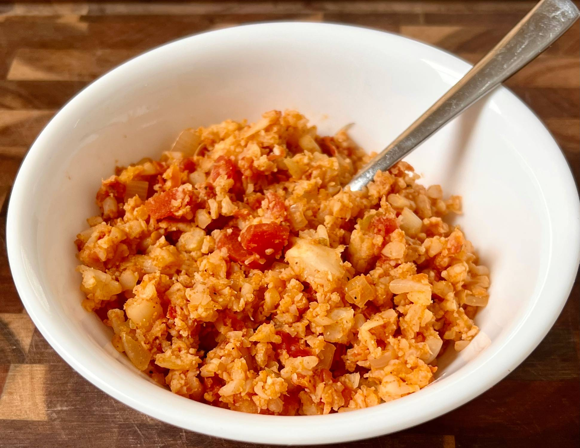 Keto Spanish rice made with cauliflower rice, Rotel tomatoes, and taco seasoning in a white bowl