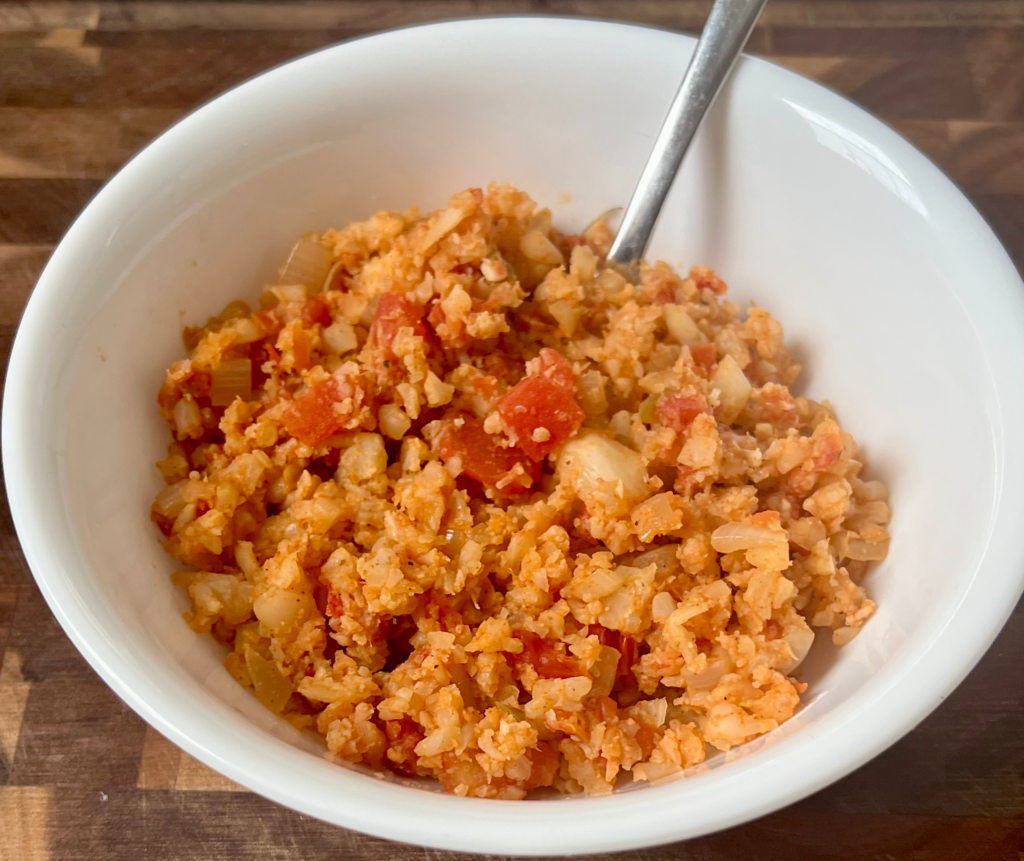 Fluffy keto Spanish cauliflower rice in a white bowl with onions and tomatoes