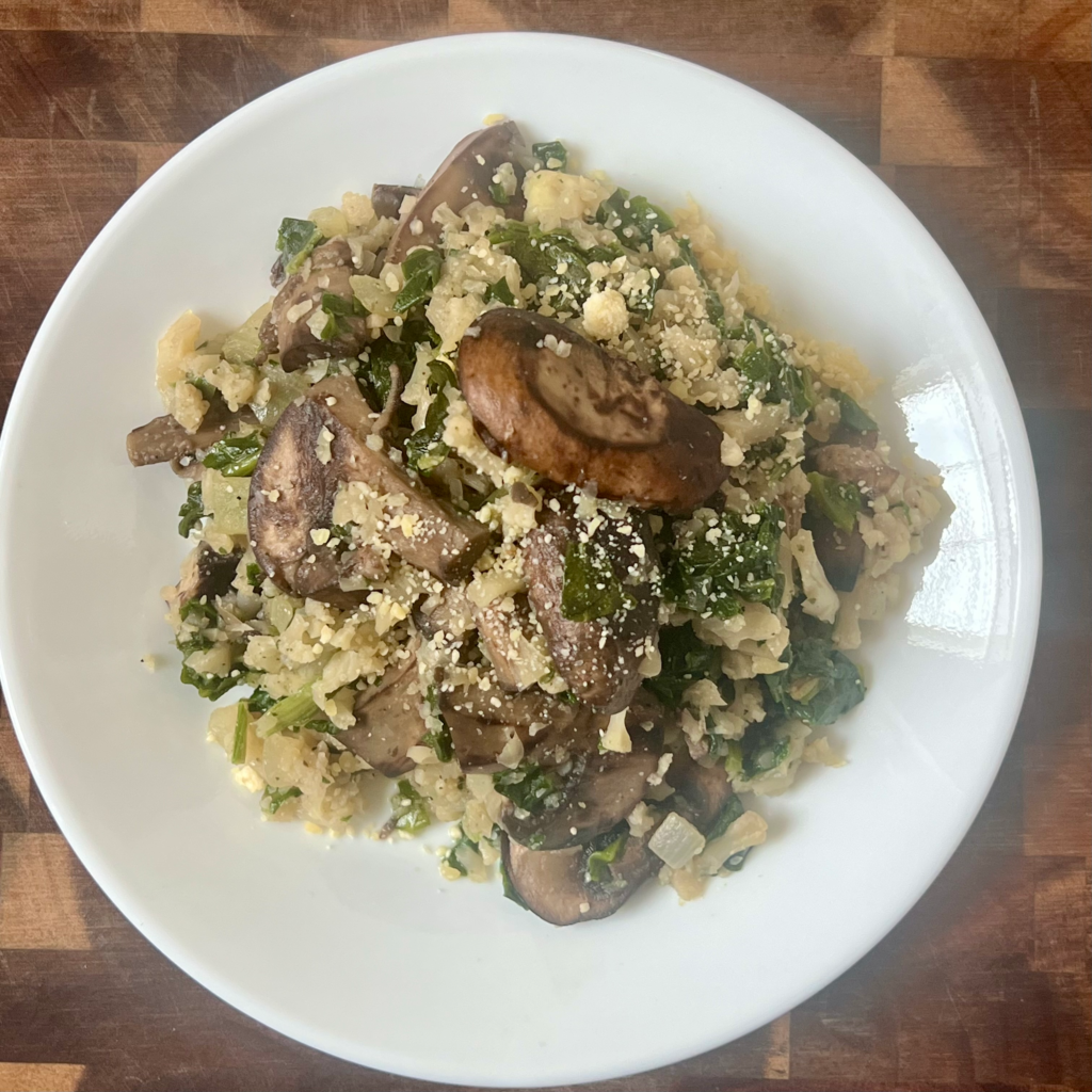 Top view of spinach mushroom cauliflower rice with mushrooms, spinach, and garlic on a white plate.