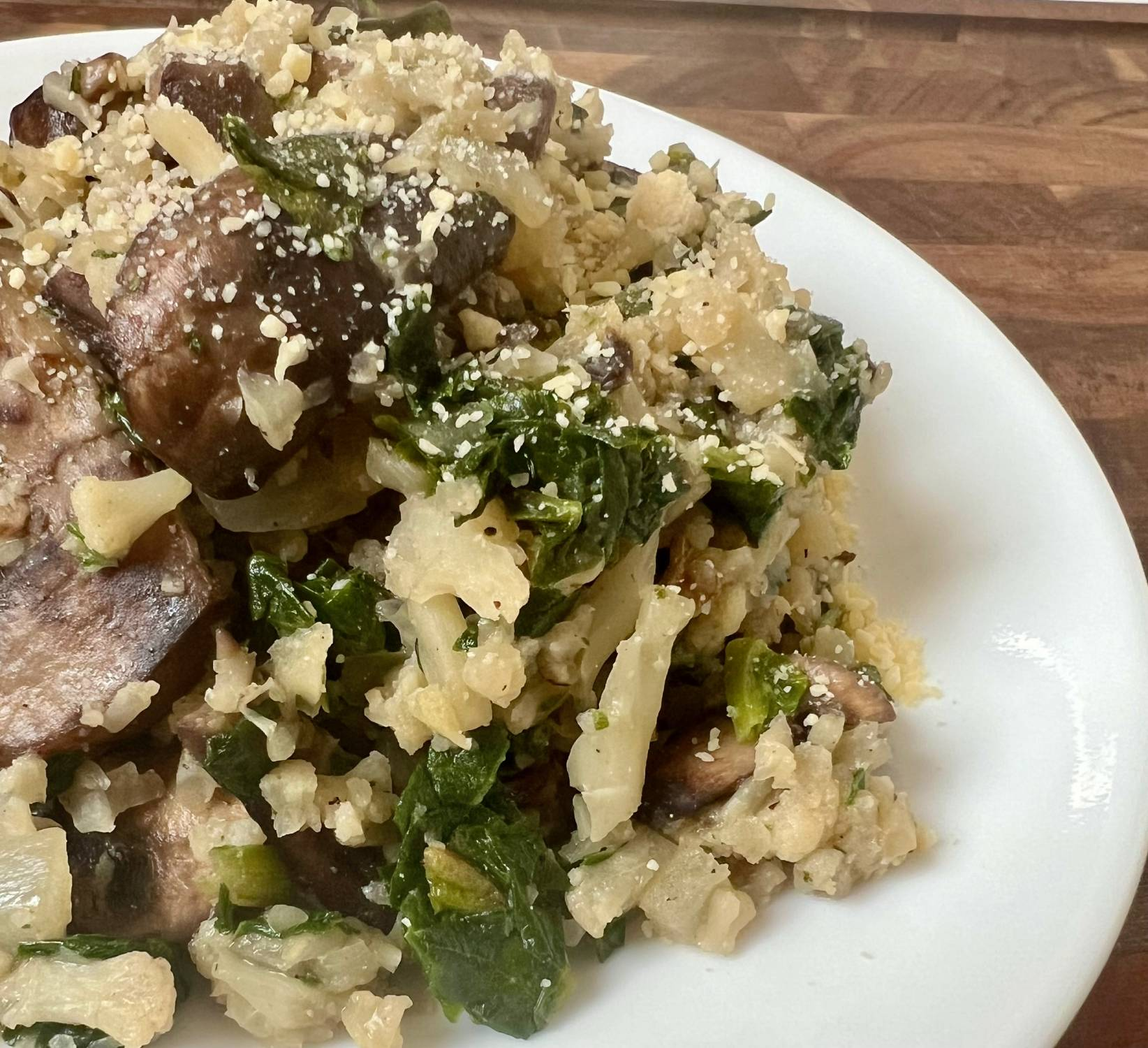 Spinach mushroom cauliflower rice topped with parmesan on a white plate, a cozy low carb side dish.