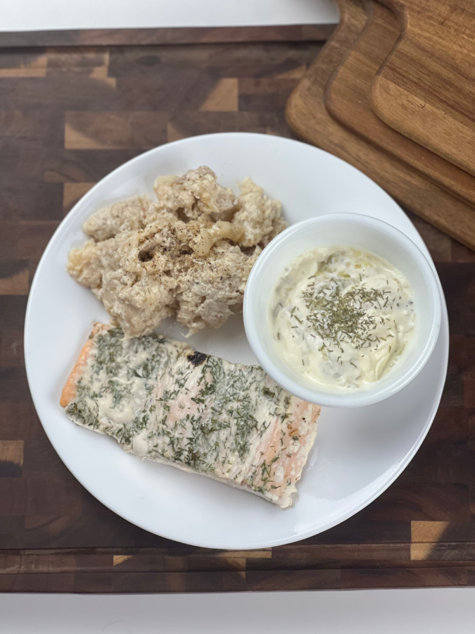 Close-up of keto baked salmon with dill mayo alongside creamy pepper jack cauliflower and a bowl of homemade keto tartar sauce.
