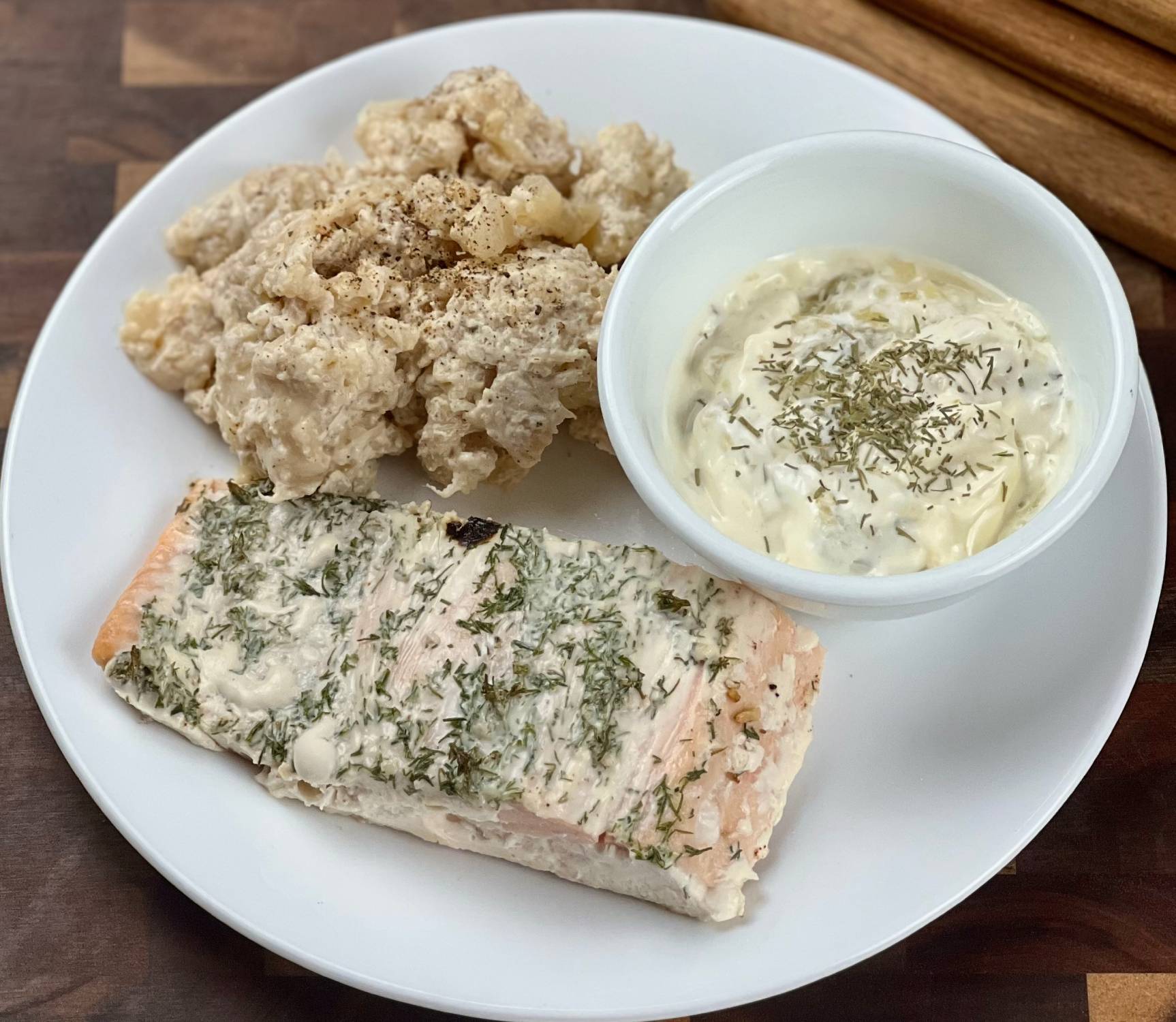 Keto baked salmon topped with creamy dill mayo served on a white plate with pepper jack cauliflower and homemade tartar sauce.