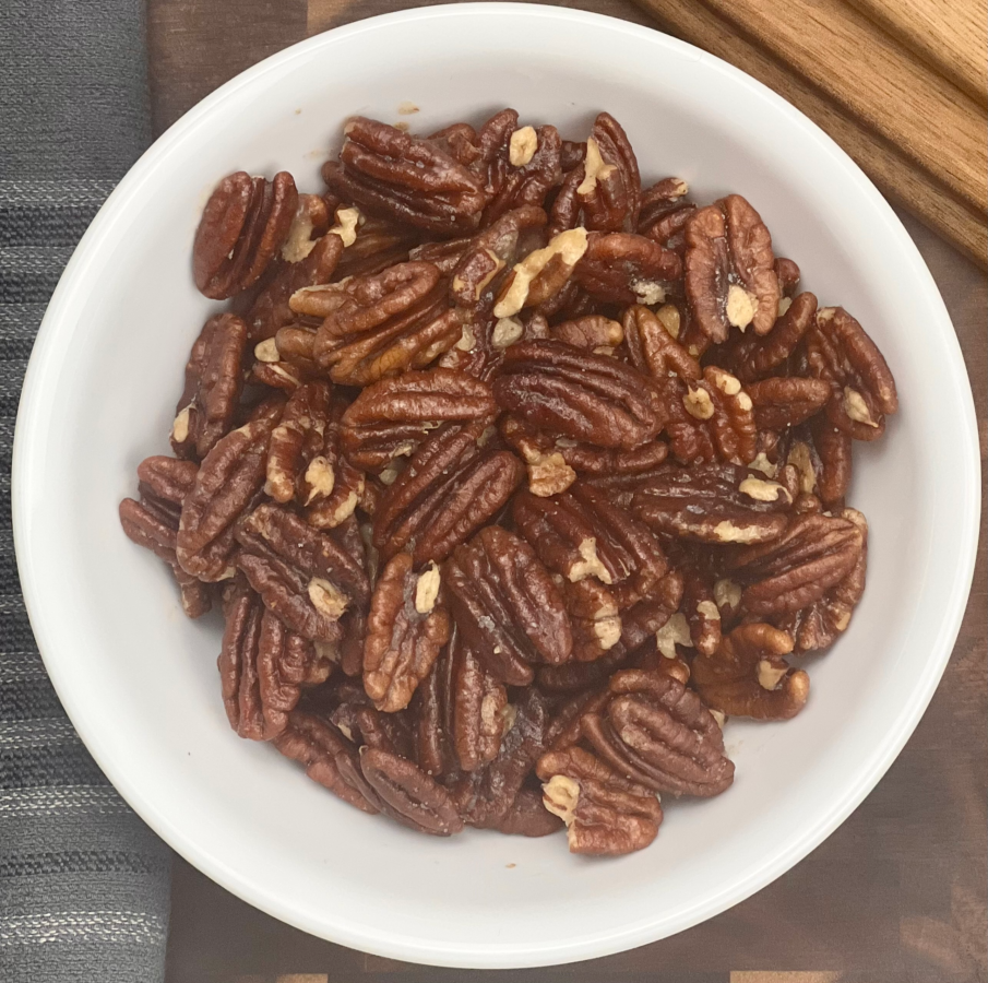 Top view of 3 ingredient keto roasted pecans in a white bowl on a wooden board.
